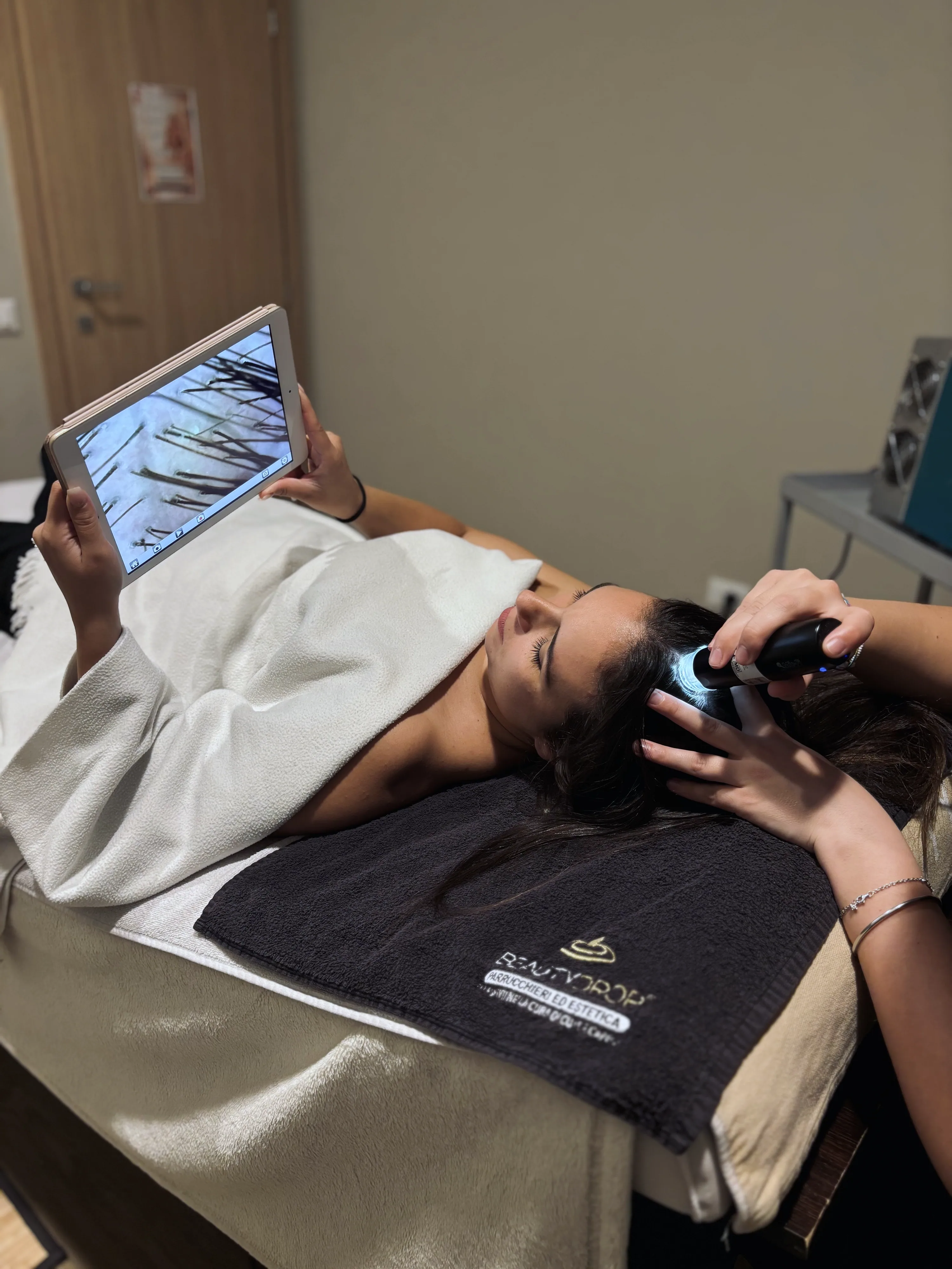 Una cliente sdraiata durante il check-up: la microcamera appoggiata sulla cute mostra i capelli ingranditi sul tablet